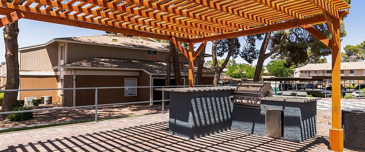 Charming outdoor patio with wooden pergola and built-in grill, perfect for entertaining in a serene residential community.