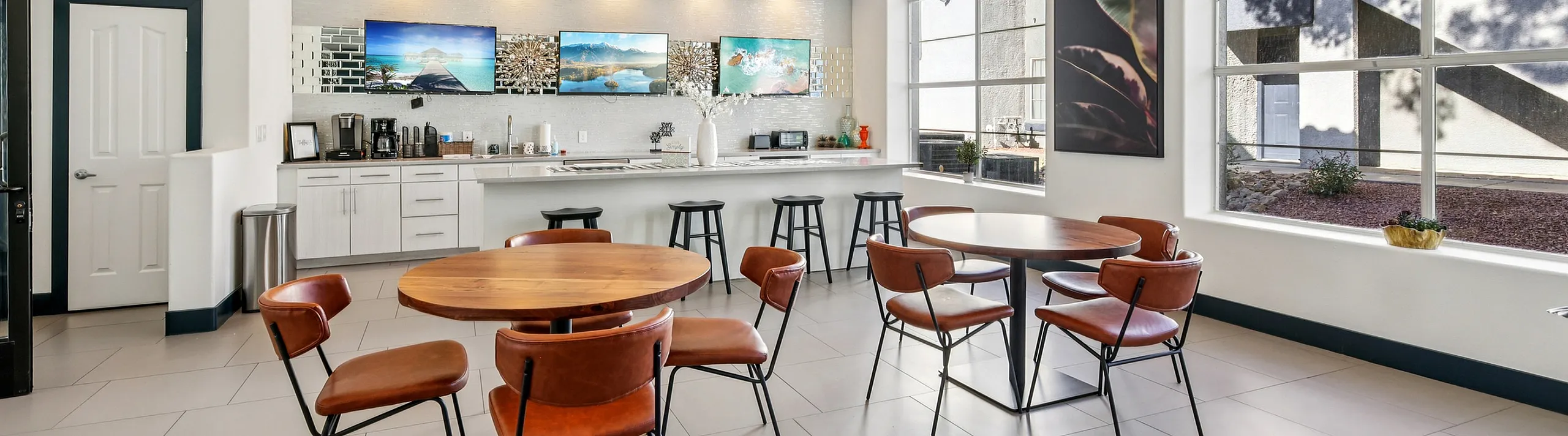 Bright communal kitchen and dining area with modern decor, stylish round tables, and large windows offering plenty of natural light.