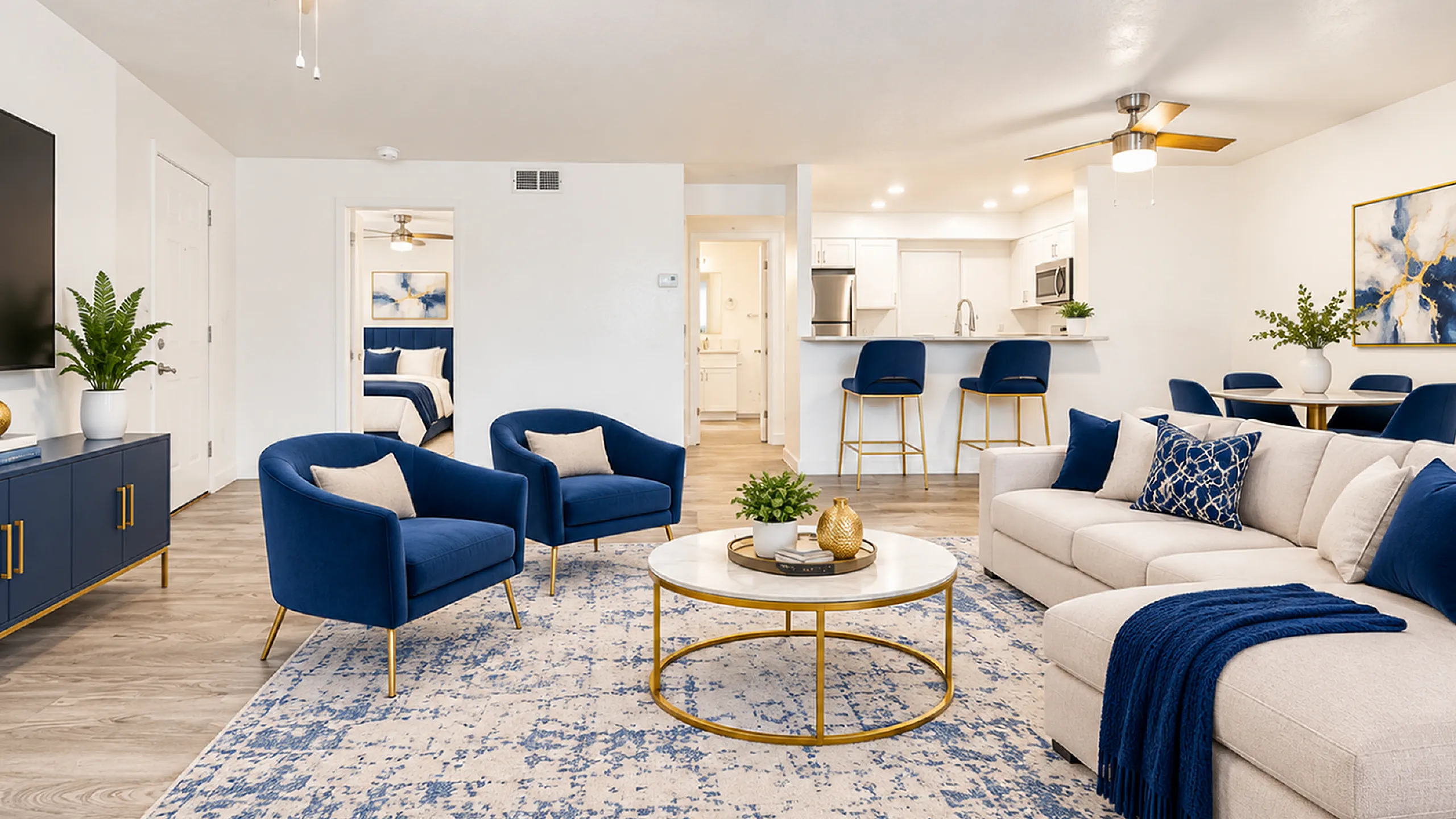 Modern open-concept living room with elegant navy and gold decor, plush seating, and a sleek kitchen with barstools.