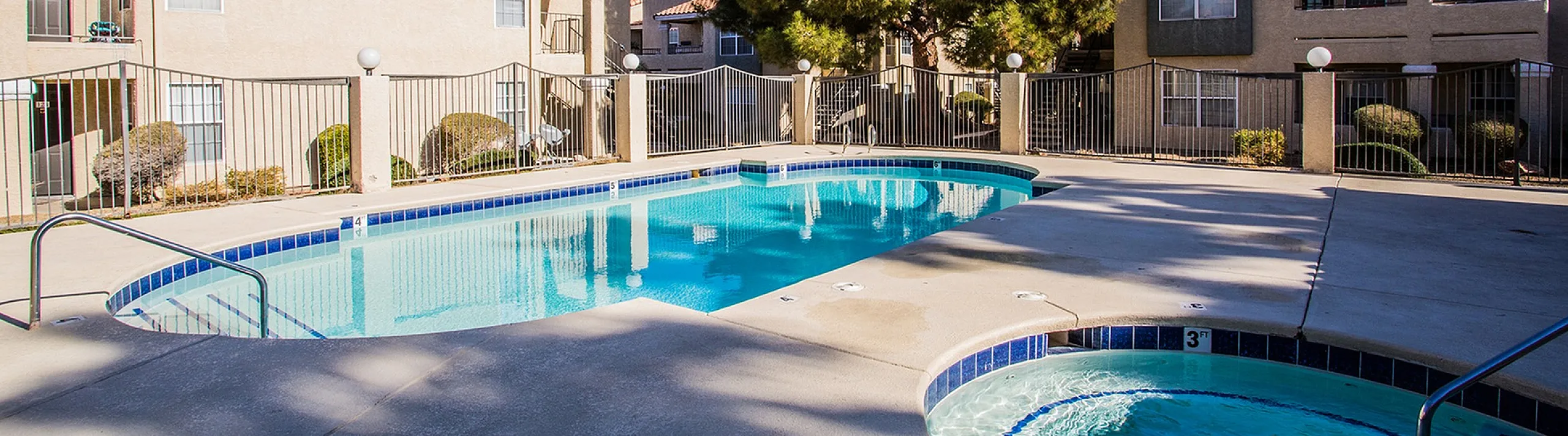 Inviting apartment complex with a sparkling pool and charming spa under a clear blue sky, surrounded by well-maintained greenery and stylish buildings.