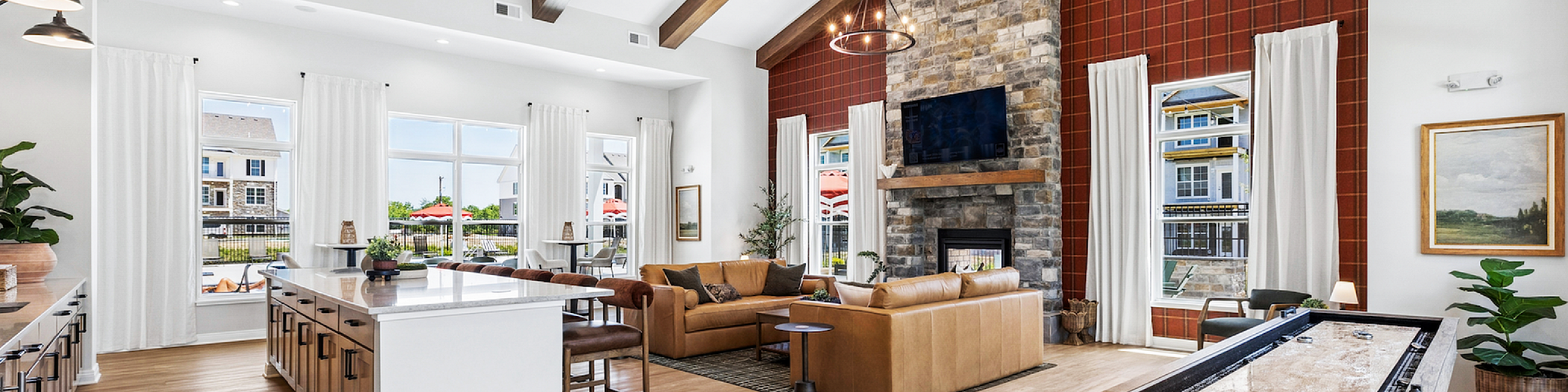 Elegant open-concept living area featuring exposed wooden beams, a stone fireplace, modern kitchen, and lounge space with large windows and natural light.