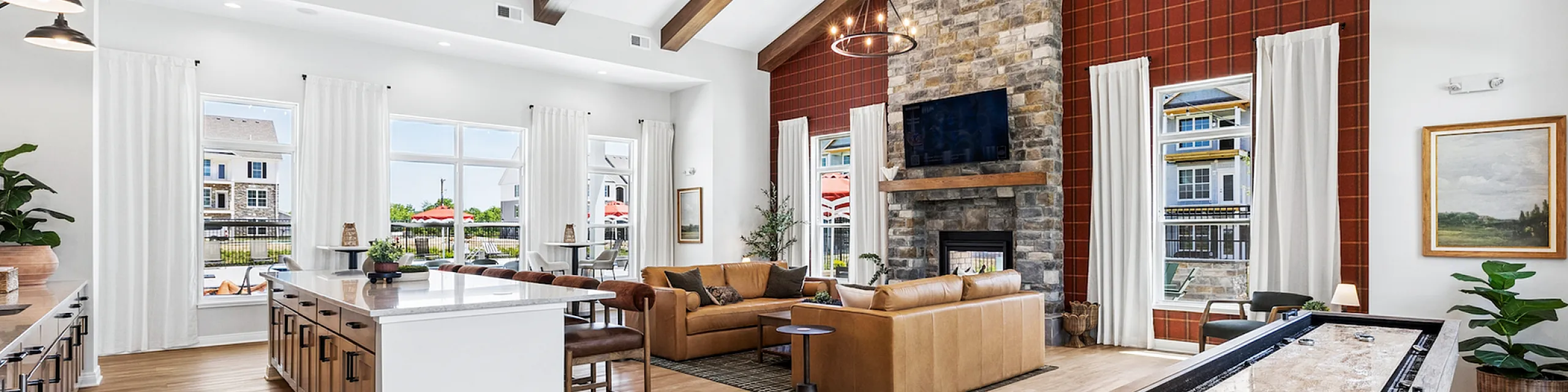 Luxurious open-concept living area featuring elegant wood-beamed ceilings, a cozy stone fireplace, and exquisite natural light from panoramic windows.
