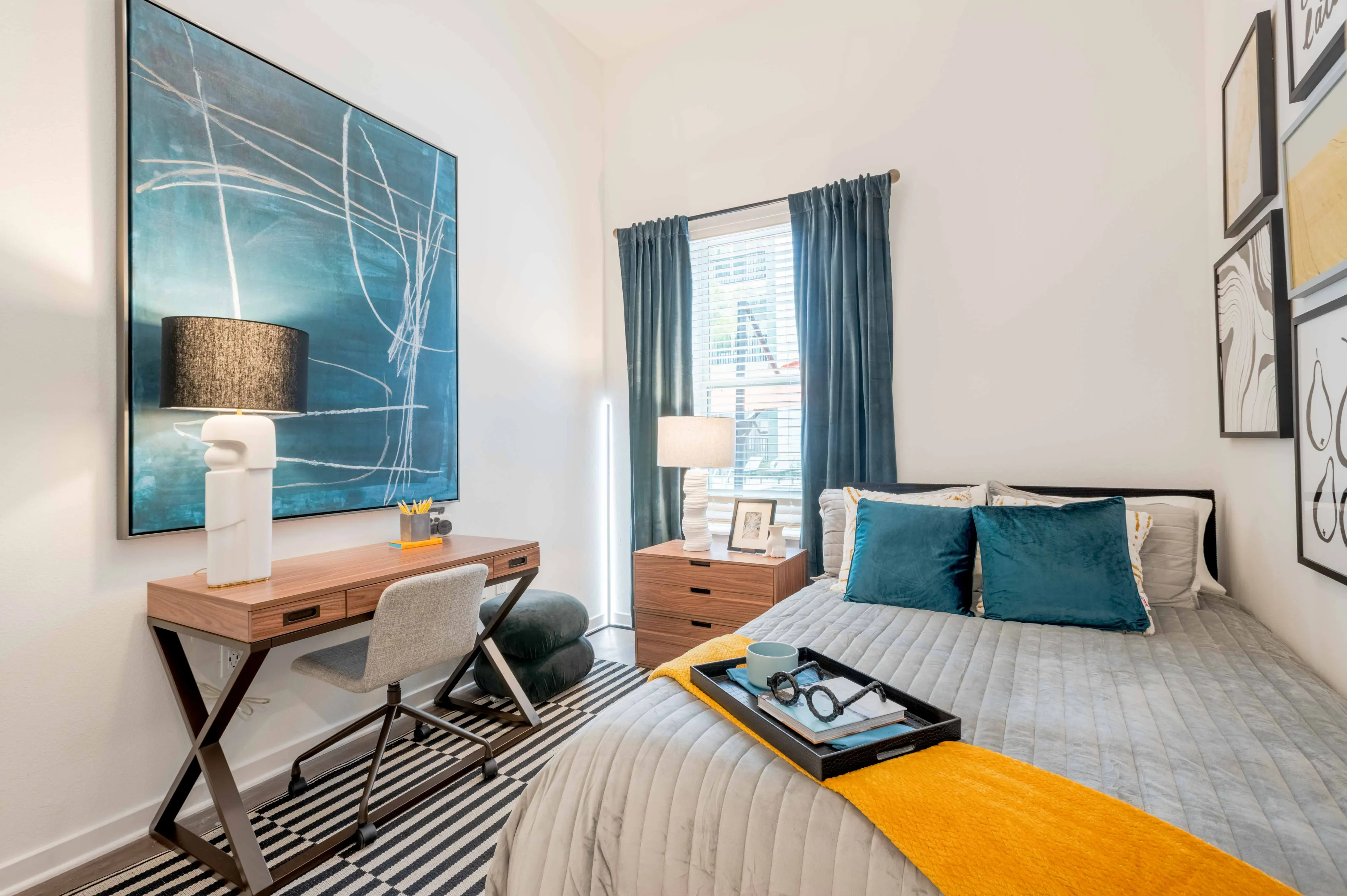 Model apartment bedroom with a full size bed, desk, chair, and dresser