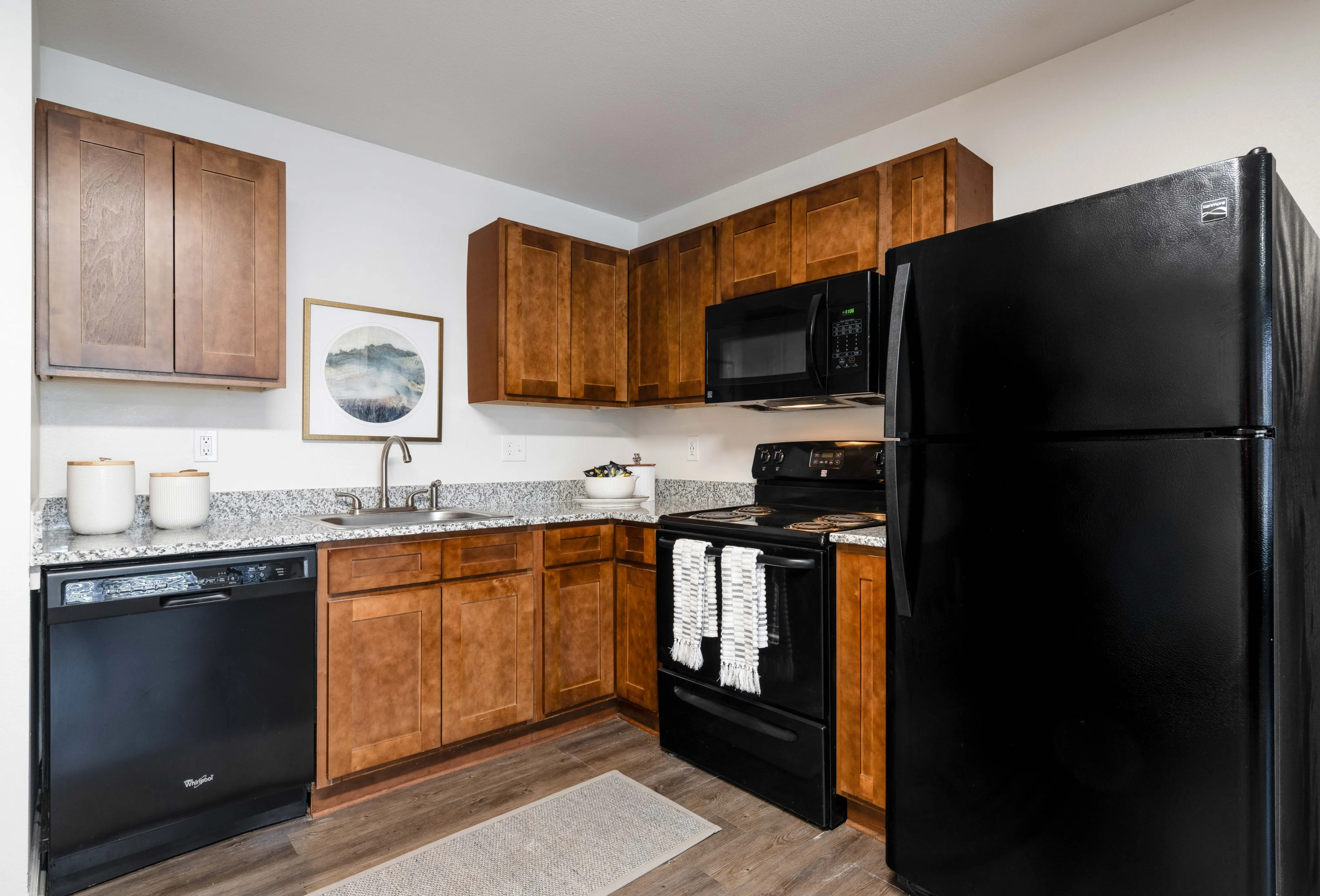 Model apartment kitchen with brown cabinets and black appliances