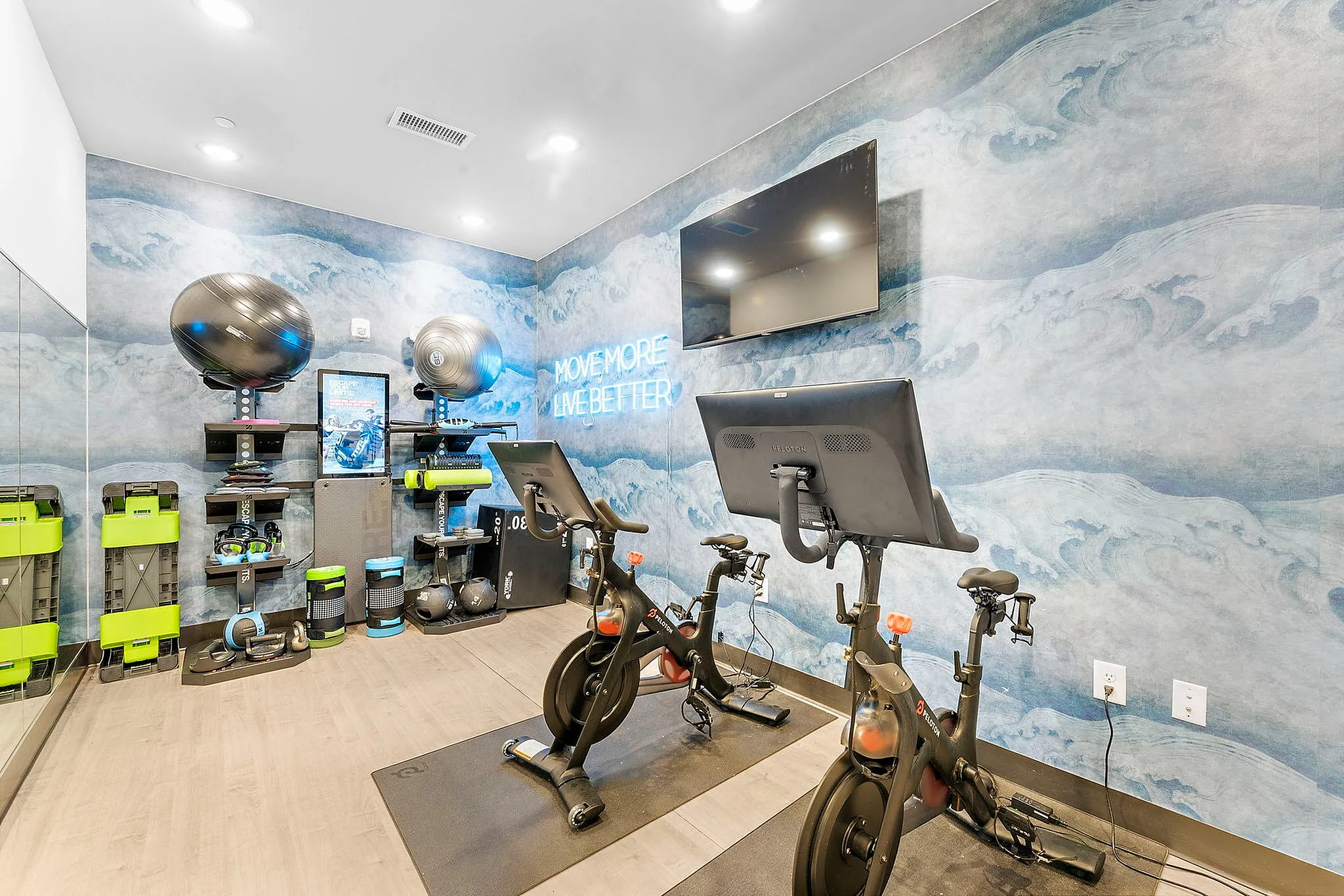 Chic home gym with modern exercise bikes, vibrant wave-patterned walls, and motivational neon sign.