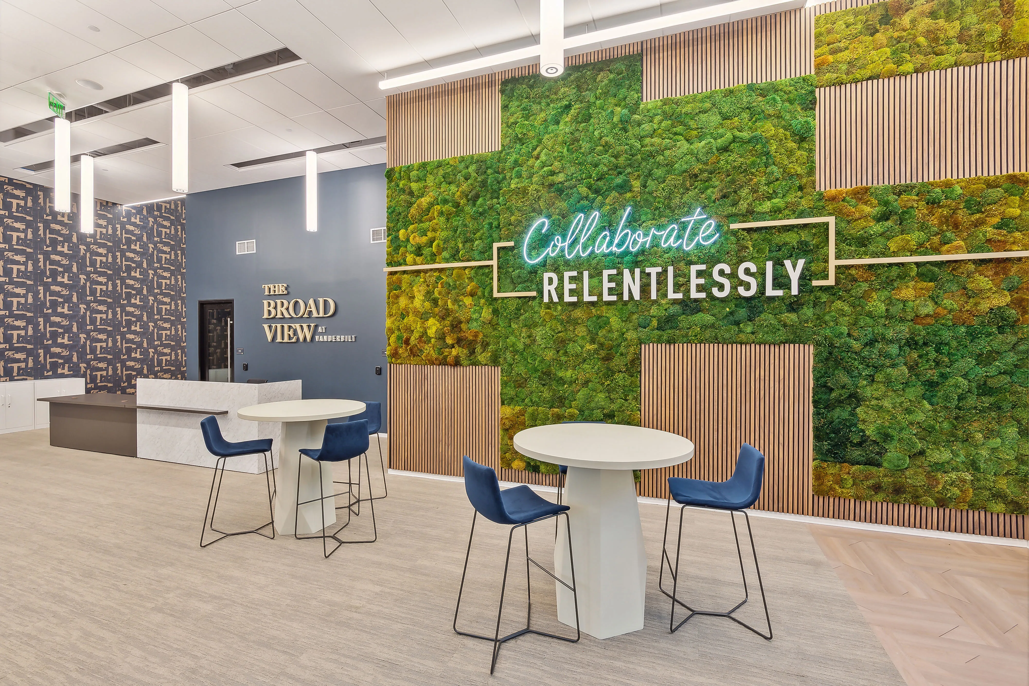 Modern coworking space with vibrant green wall, stylish seating, and inspiring \'Collaborate Relentlessly\' neon sign.