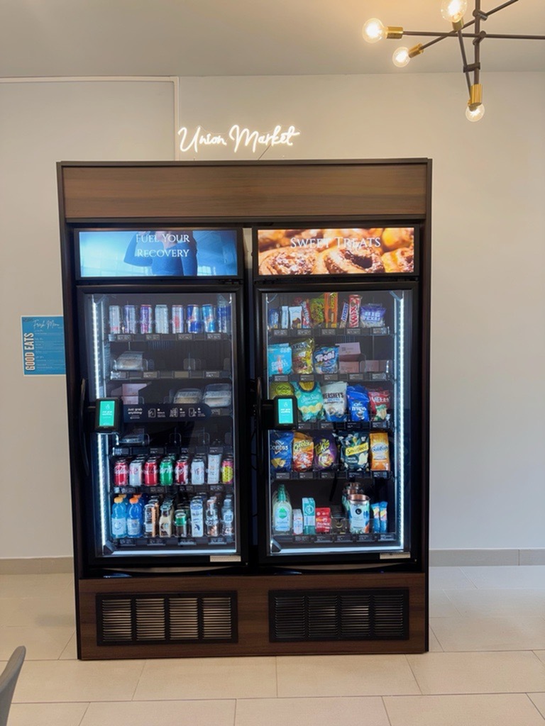 Modern snack and beverage vending machine at Union Market, offering a variety of drinks and sweet treats under warm lighting.