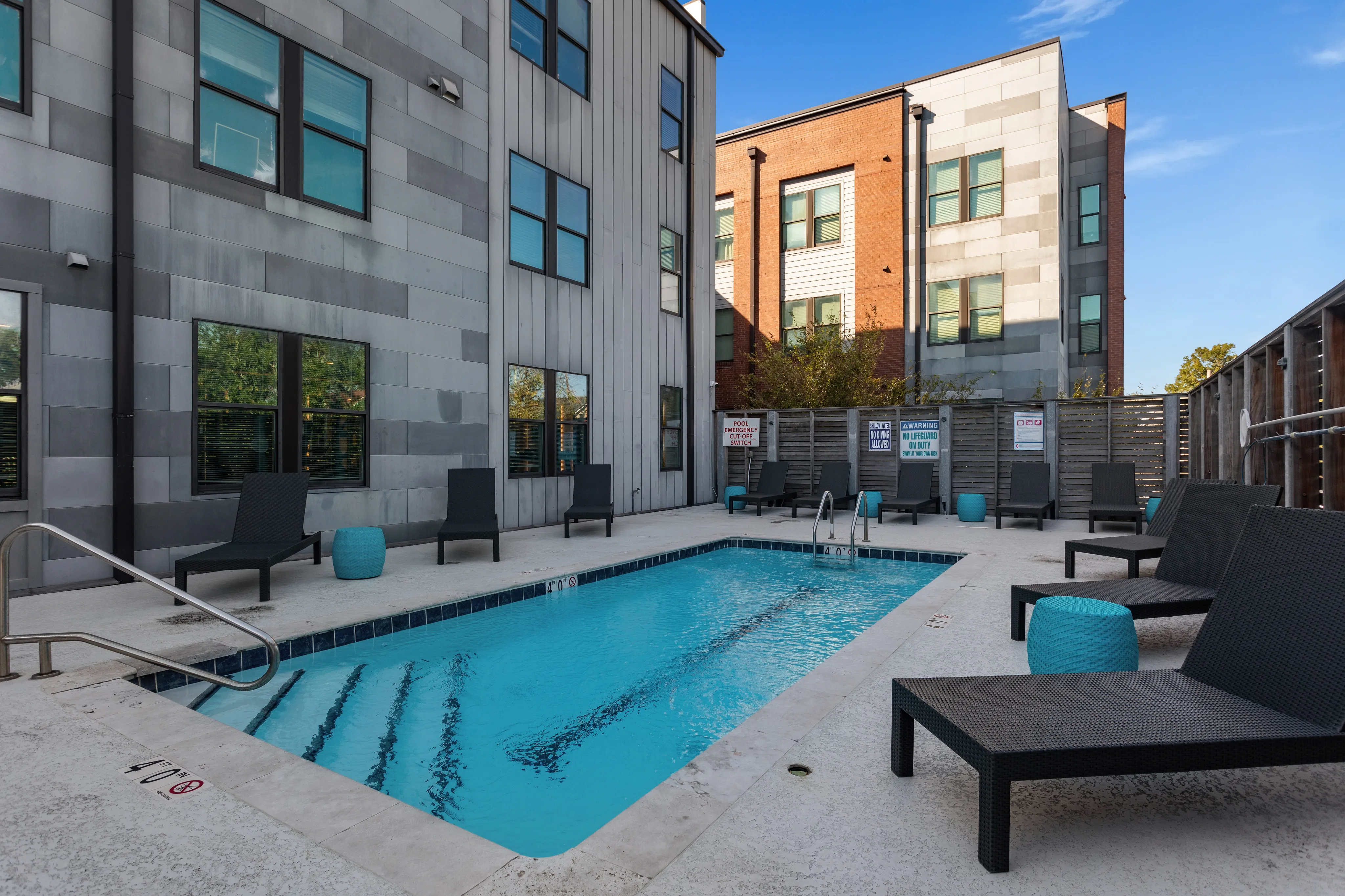 Modern apartment complex with stylish outdoor pool area, comfortable lounge chairs, and vibrant blue accents.