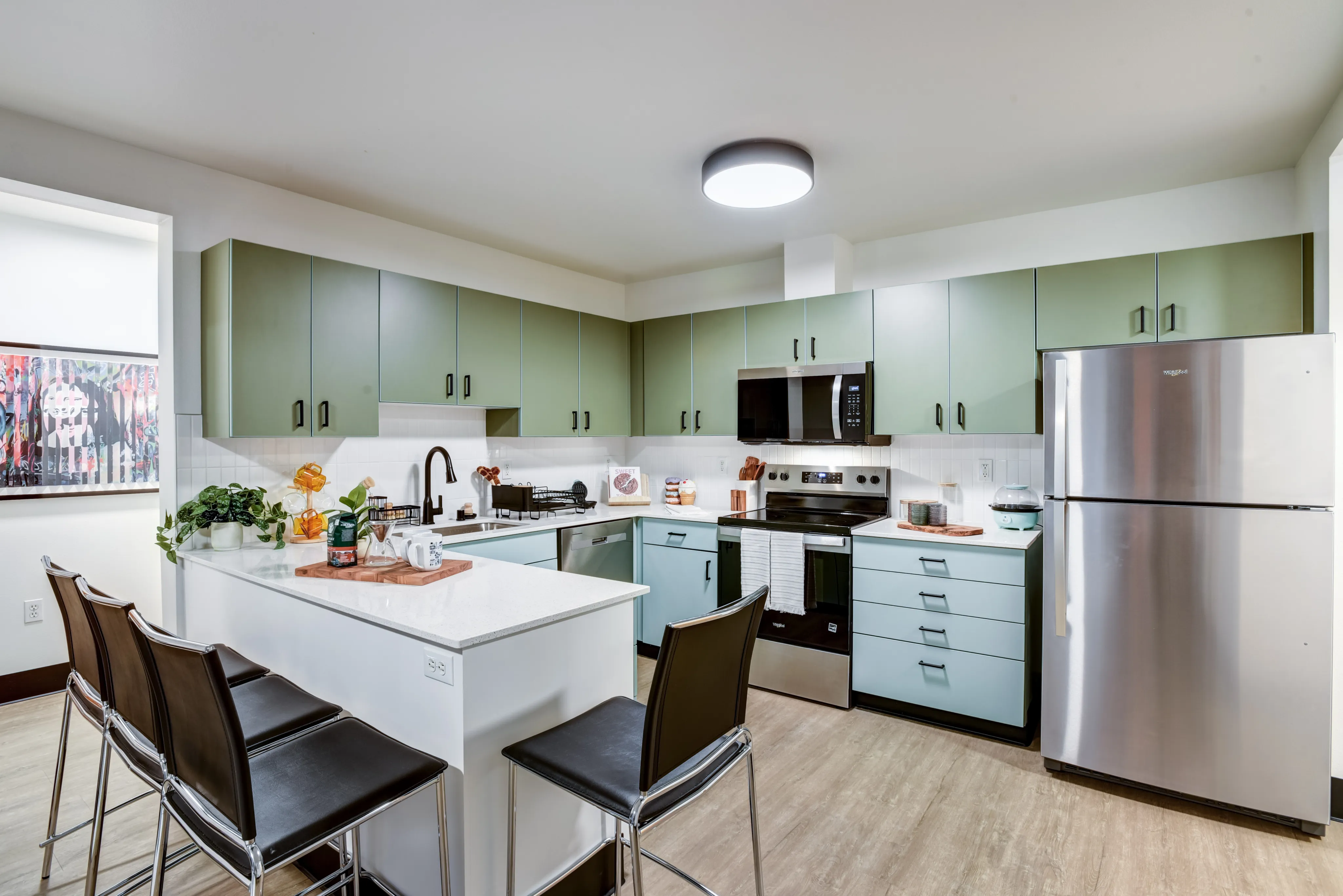 Modern kitchen with sleek green cabinetry, stainless steel appliances, and a stylish island featuring comfortable bar stools.
