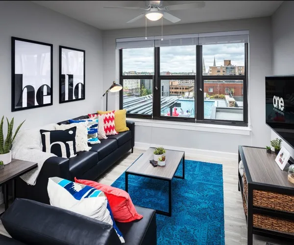 Model living room at One On Centre Apartments in Pittsburgh, PA, featuring wood grain flooring and a black couch.