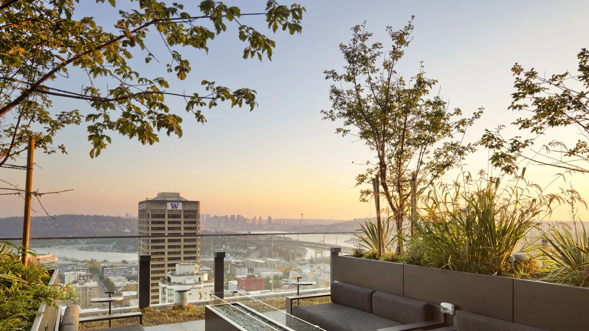 Rooftop lounge space with couches and a firepit, all looking over at the city of Seattle