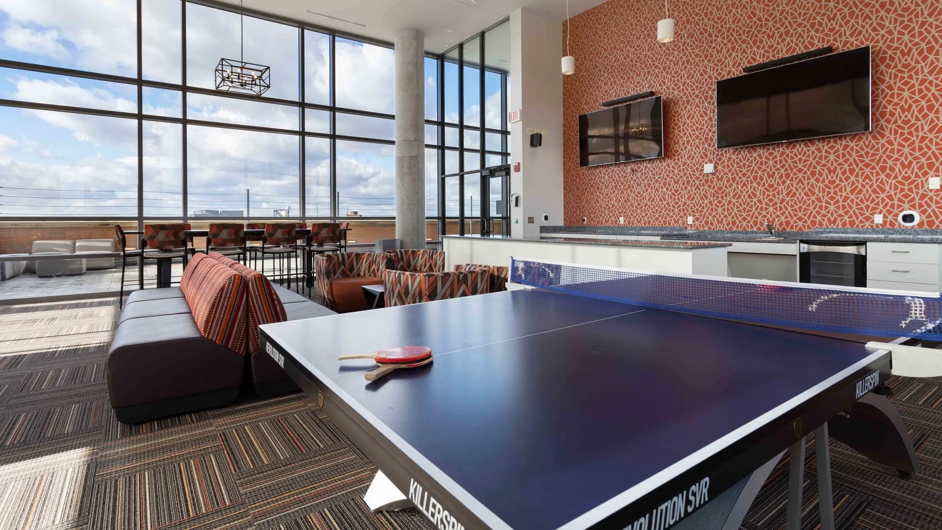 Clubhouse with pink pong table and couches facing flat screen tvs