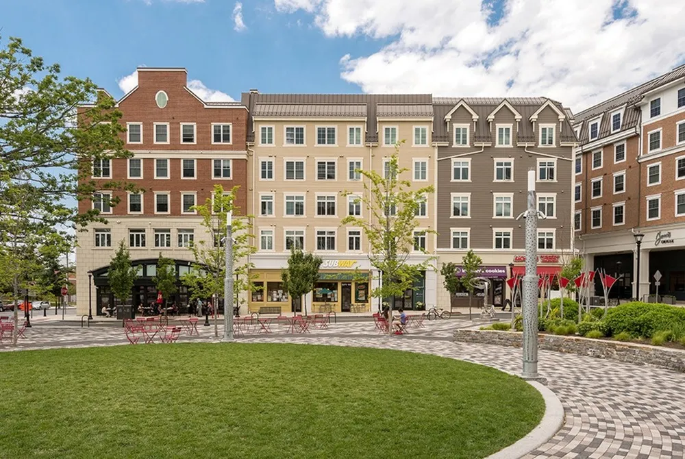Exterior view of The Oaks on the Square apartments in Storrs, CT, featuring a green lawn and outdoor seating.