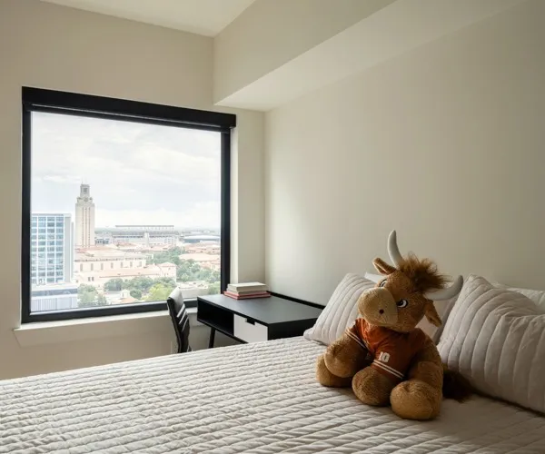 Model apartment bedroom with full size bed, desk, and chair with a large window looking out at the city of Austin