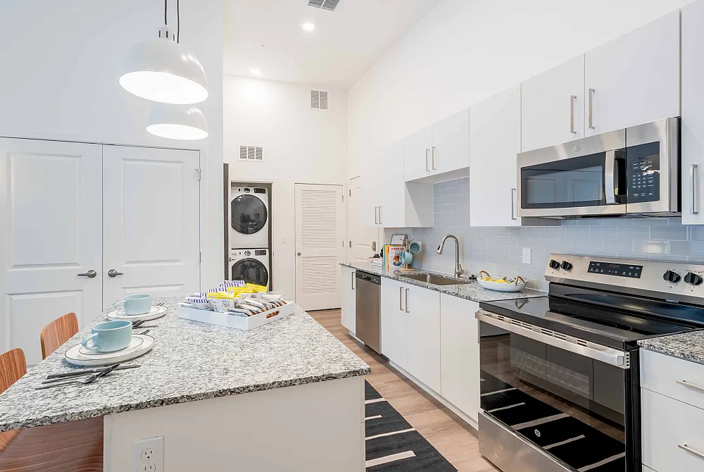Model apartment kitchen with granite counter tops, white cabinets, and stainless steel appliances