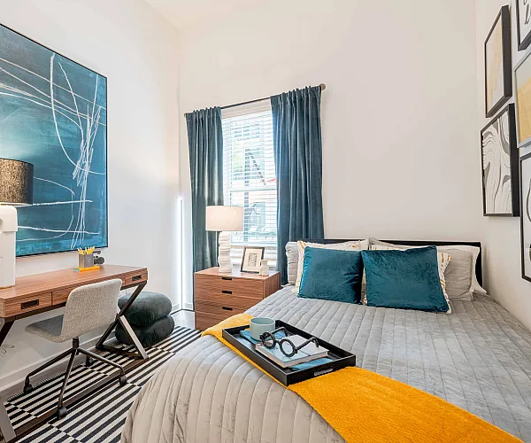 Model apartment bedroom with a full size bed, desk, chair, and dresser