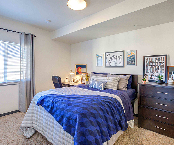 Model apartment bedroom with a full size bed, dresser, desk, and desk chair