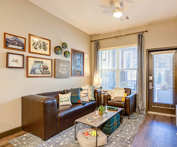 Model apartment living room with a couch, arm chair, and coffee table facing a flat screen tv