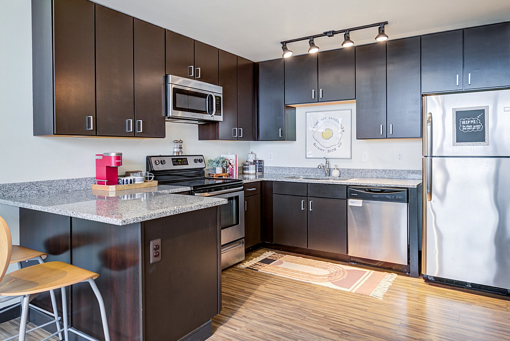 Model apartment kitchen with dark brown cabinets, stainless steel appliances, and granite countertops