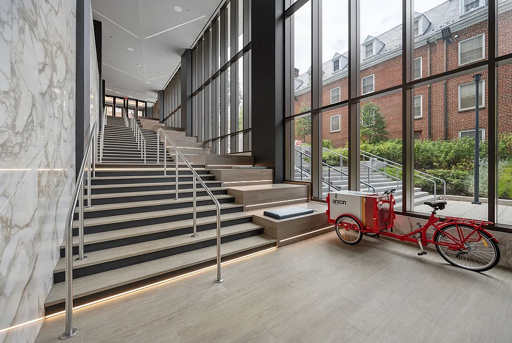 An interior view of an indoor space at Union on Knox's College Park, MD apartments featuring stairs with railings and floor to ceiling windows, and a red bicycle situated near the windows.