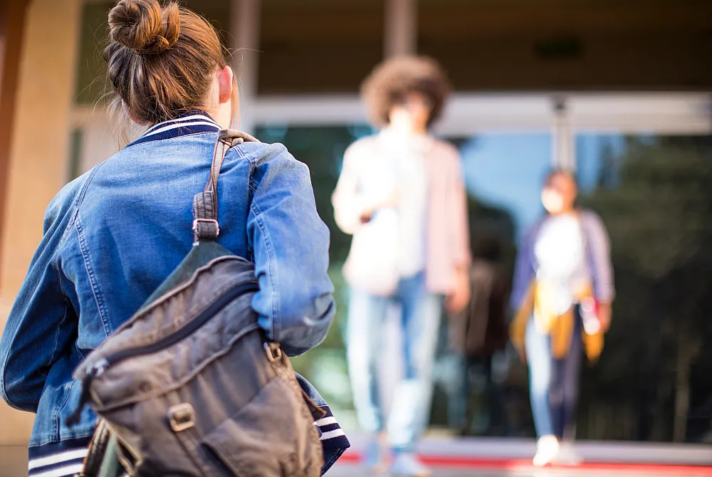 Stock photo of someone with a backpack on walking up to a University building