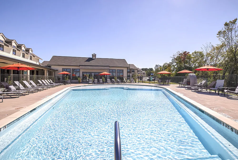 Inviting apartment complex pool area with sun loungers and vibrant red umbrellas under a clear blue sky.