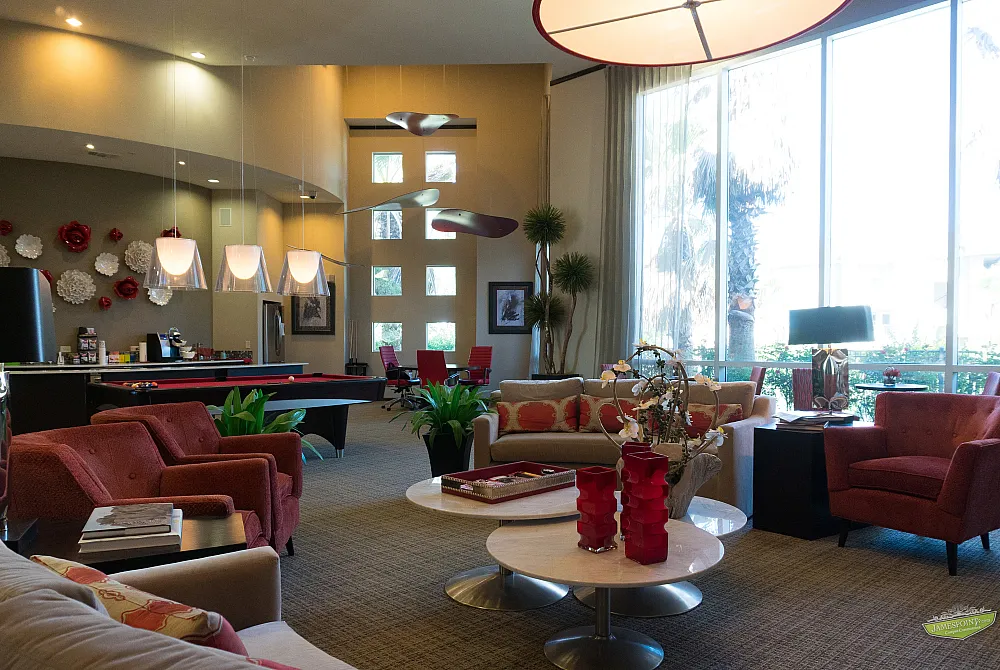 Luxurious lounge area with modern decor, featuring vibrant red seating, stylish pool table, and large windows overlooking lush greenery.