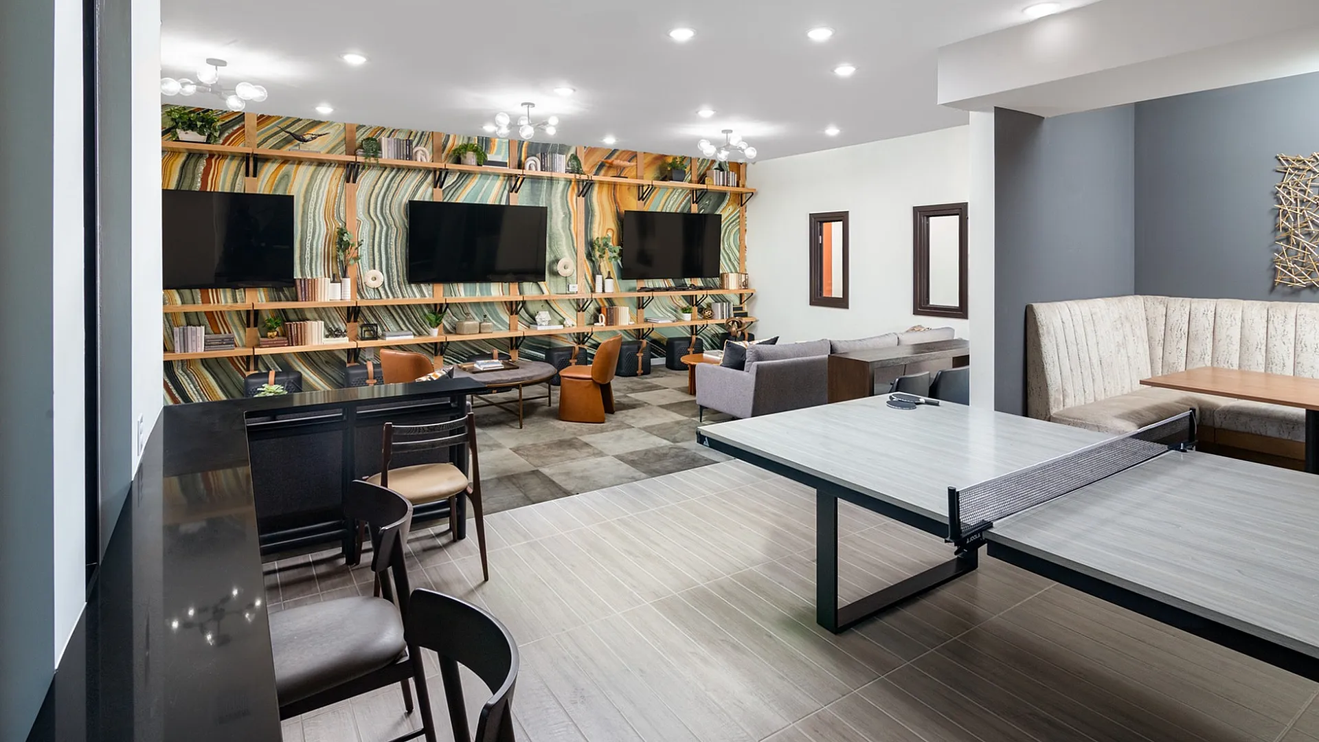 Contemporary lounge area featuring vibrant accent wall, multiple flat-screen TVs, comfortable seating, and a chic ping pong table for recreation.