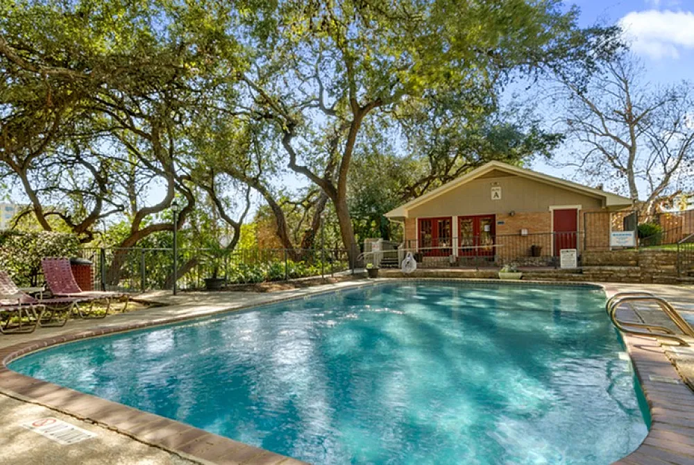 Charming outdoor swimming pool surrounded by lush trees and a cozy clubhouse, perfect for relaxation and summer fun.