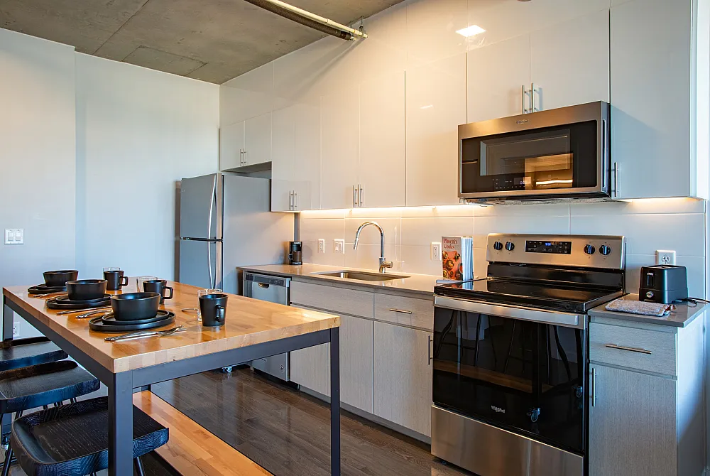 Modern kitchen boasting sleek stainless steel appliances, elegant cabinetry, and a stylish wooden dining table with chic black dinnerware.