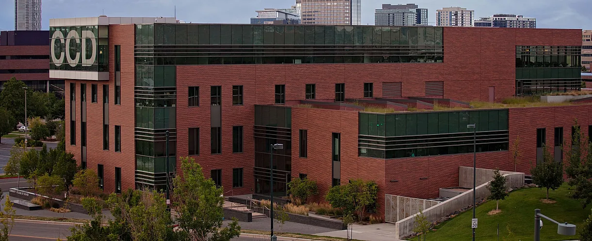 Contemporary brick building with sleek glass windows, surrounded by lush greenery and situated in a vibrant urban setting.
