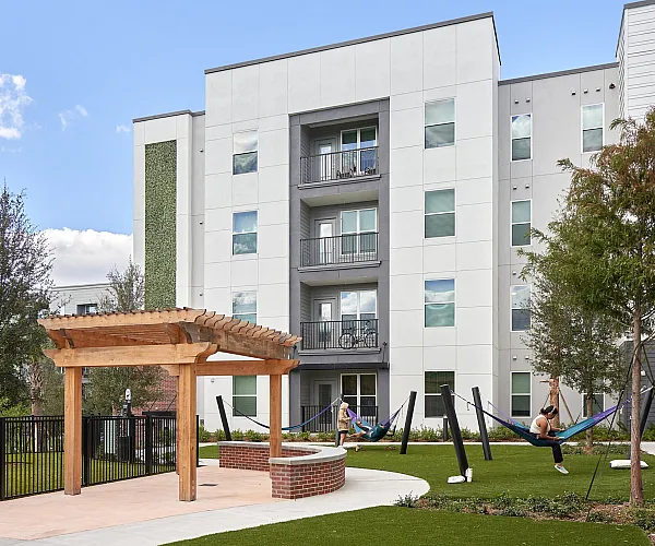 Tranquil apartment courtyard with modern architecture, lush green lawns, and inviting hammock relaxation area.