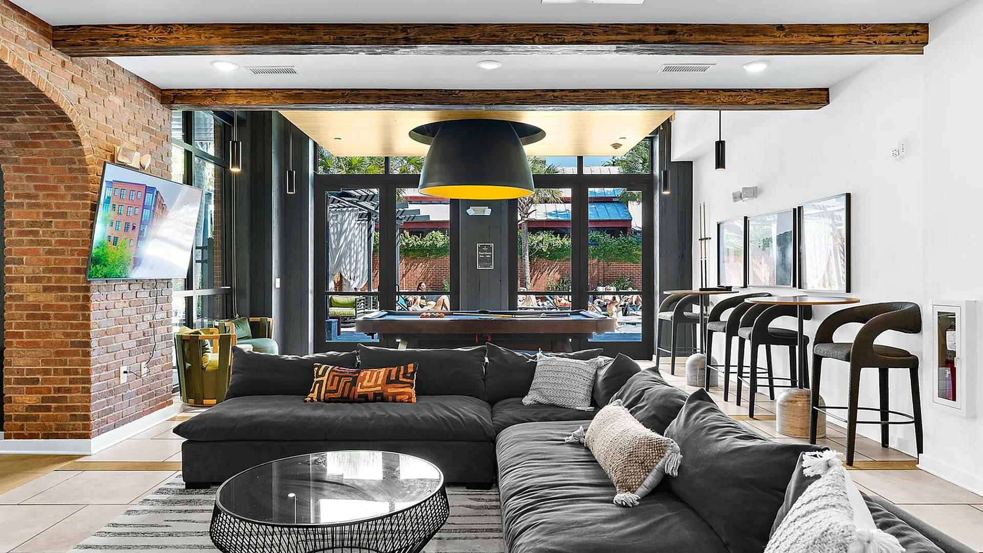 Chic living room featuring an elegant L-shaped sofa, stylish bar seating, exposed brick accents, and a large window view.