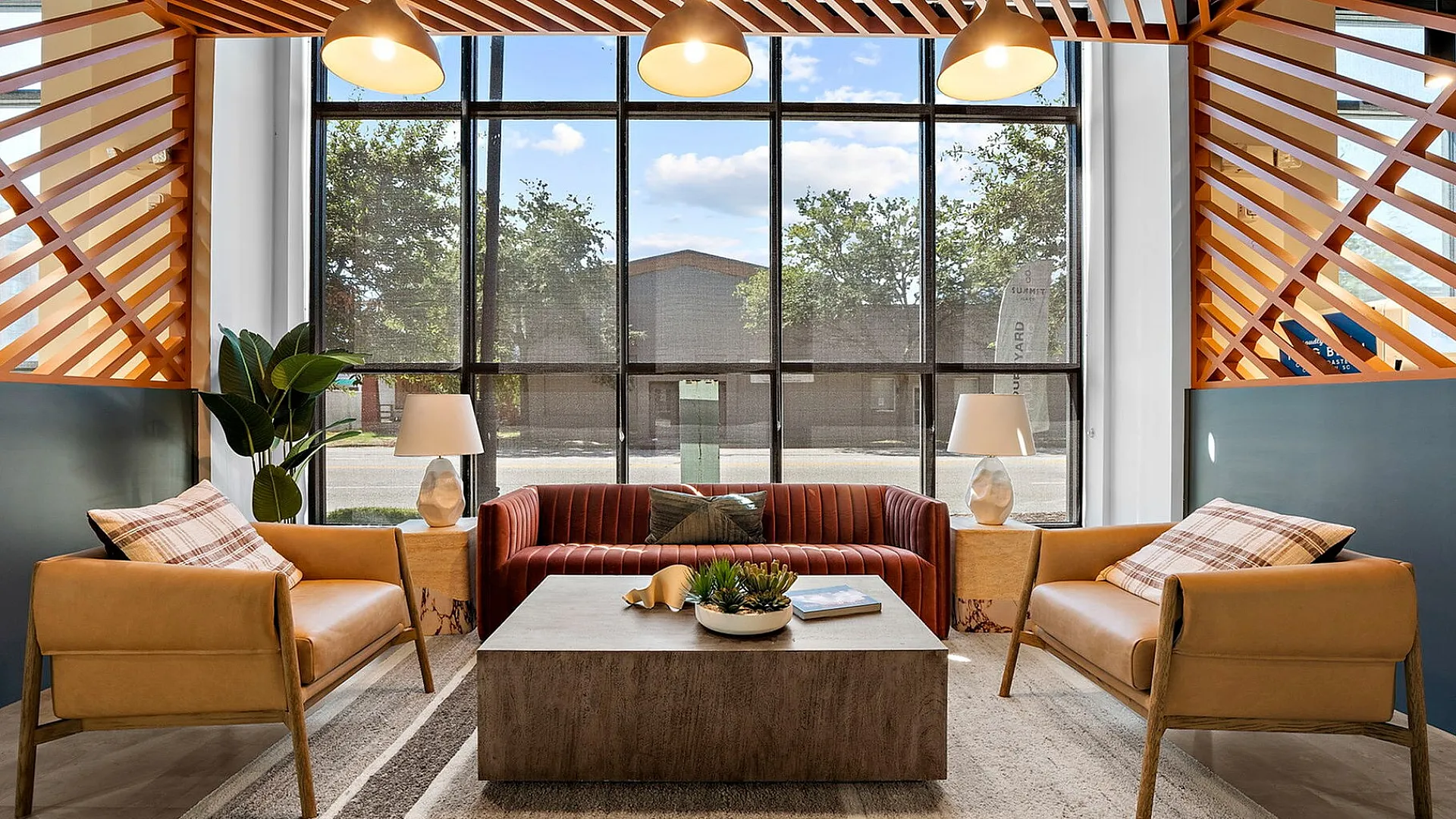 Modern living room featuring large windows, stylish seating area with leather chairs, vibrant throw pillows, and a contemporary coffee table under elegant pendant lighting.