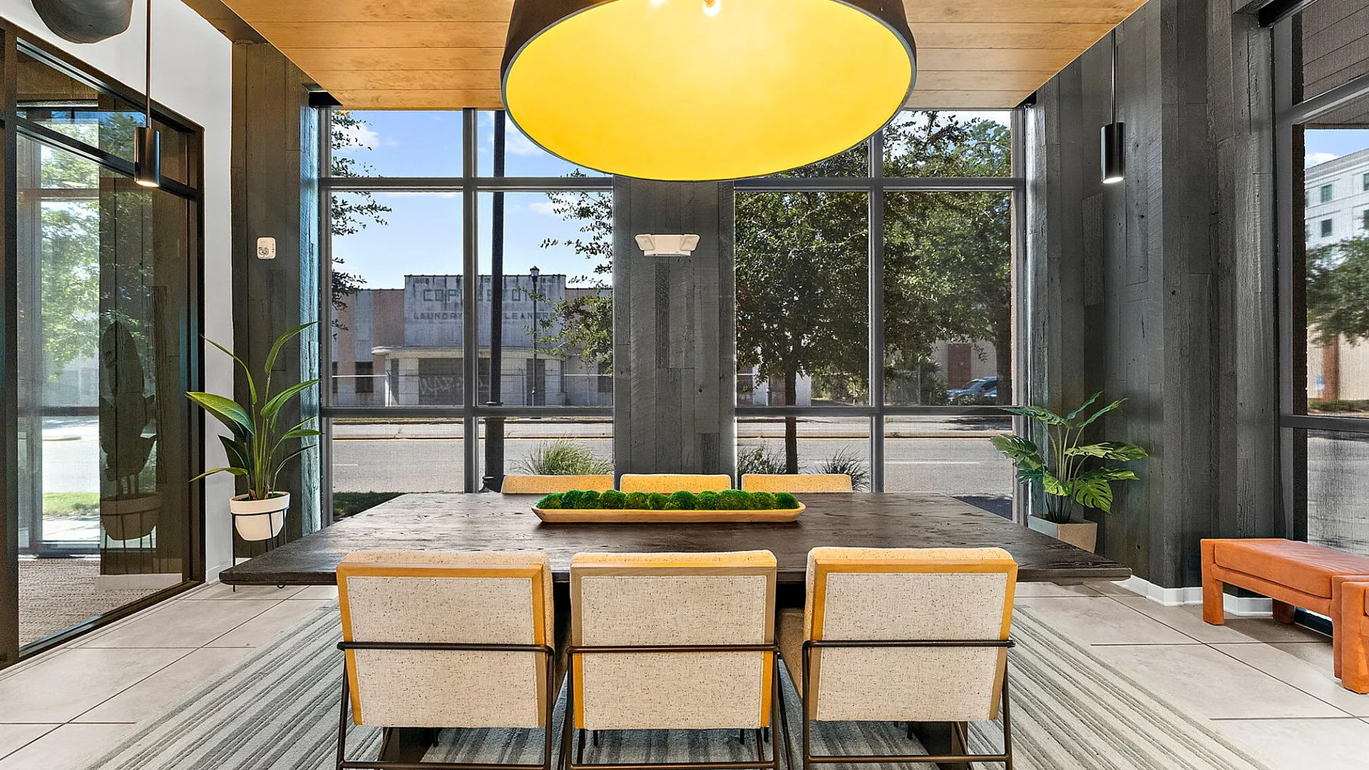 Chic dining area with a modern table, stylish chairs, large pendant light, and floor-to-ceiling windows offering natural light and greenery views.