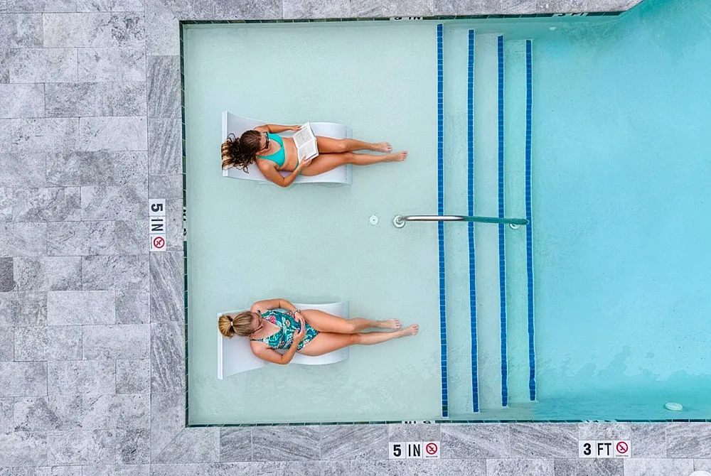 Luxurious poolside retreat with two women relaxing on in-water lounge chairs, surrounded by elegant stone tiling.