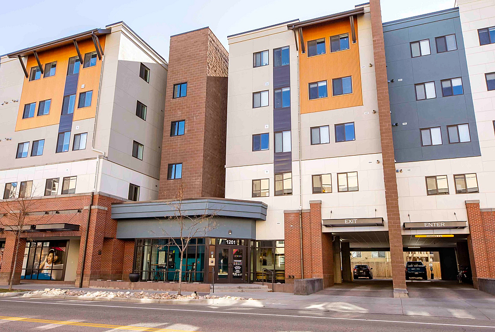 Modern urban apartment complex featuring a vibrant facade with large windows, convenient street-level entrances, and ample parking access.
