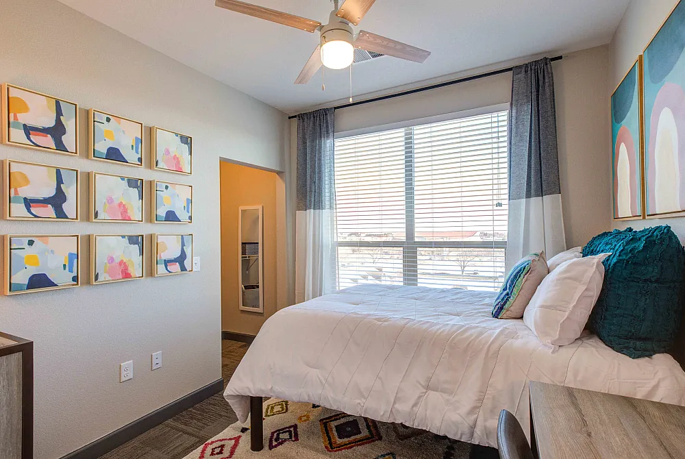 Bright and inviting bedroom with modern art decor, plush bedding, and large window for natural light.