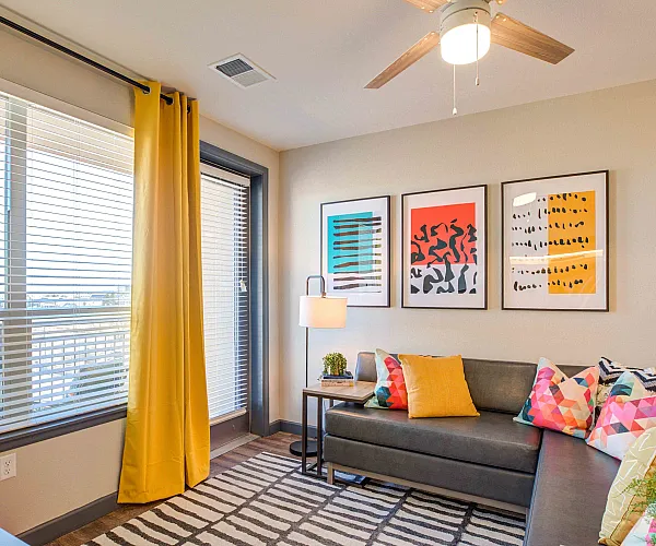 Vibrant living room with colorful decor, featuring a cozy sectional sofa, abstract wall art, and large windows with yellow curtains.