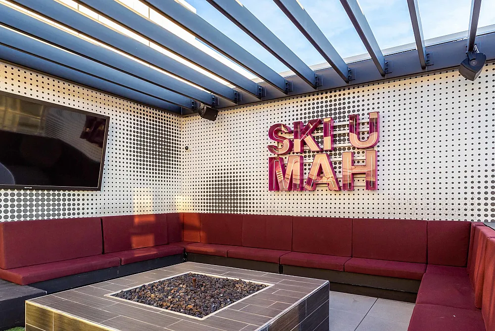 Chic outdoor lounge with maroon sectional seating, sleek firepit, and stylish wall art under a modern pergola.