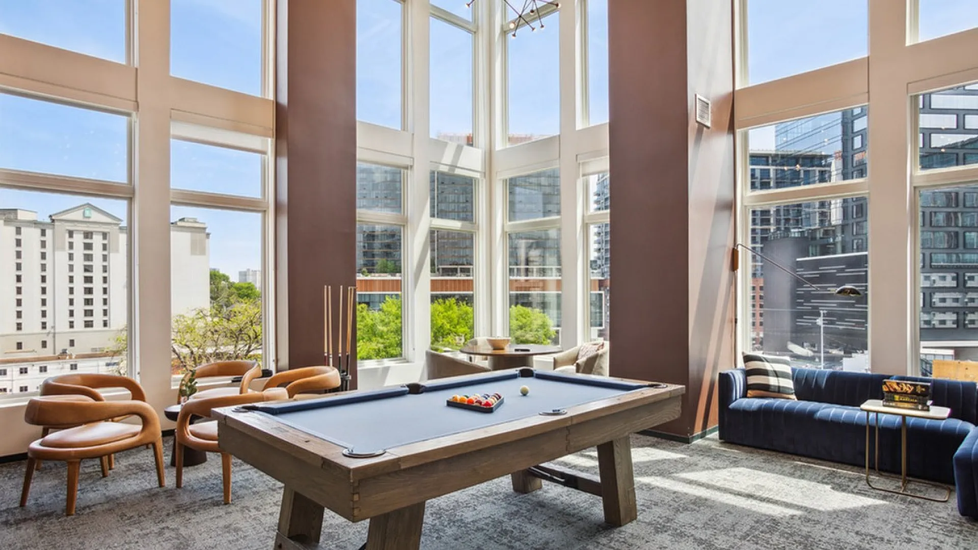 Luxurious apartment lounge featuring a stylish pool table, floor-to-ceiling windows with city views, and chic seating arrangements.