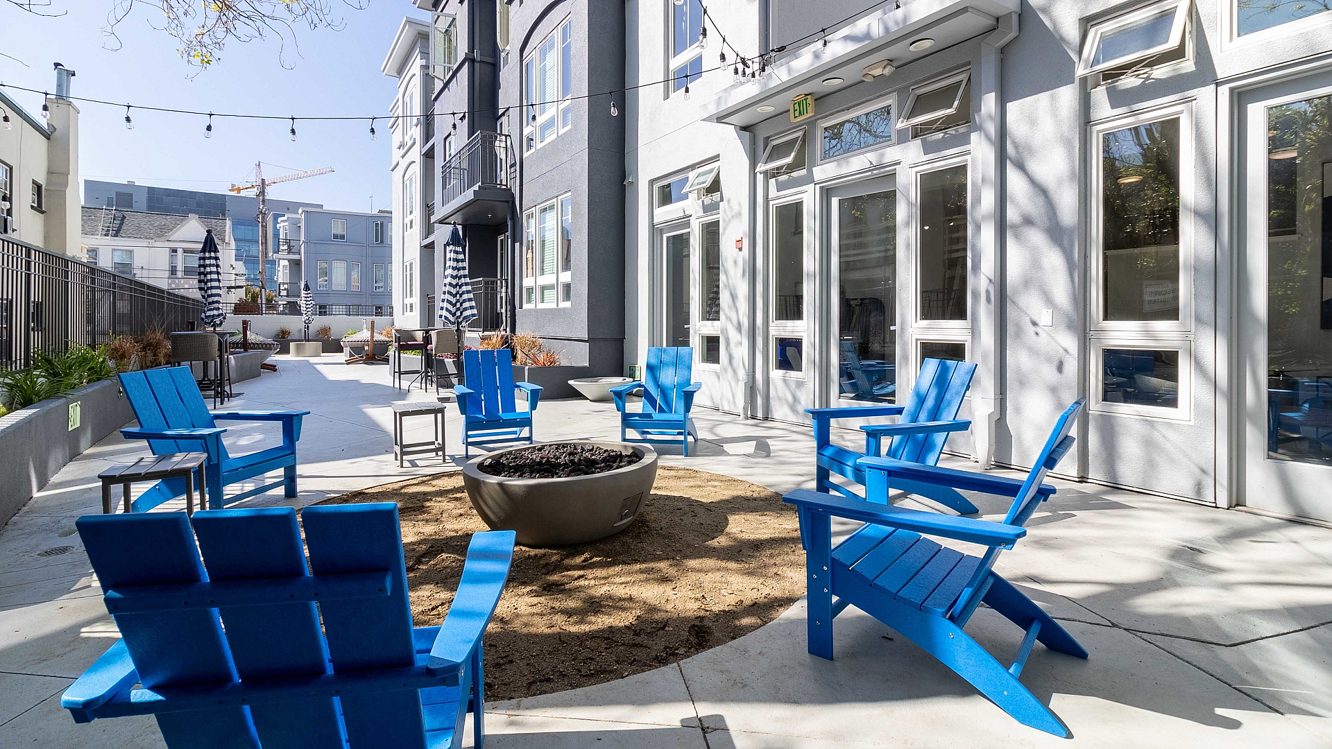 Inviting outdoor seating area with vibrant blue chairs and a cozy fire pit, nestled alongside a modern apartment building.