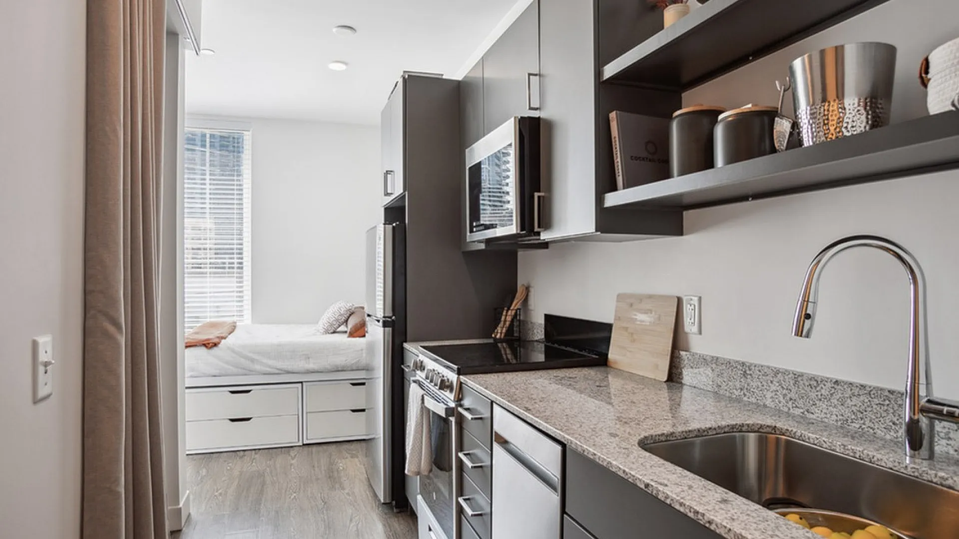 Modern kitchen with sleek cabinetry, granite countertops, and view into cozy bedroom, perfect for urban living.