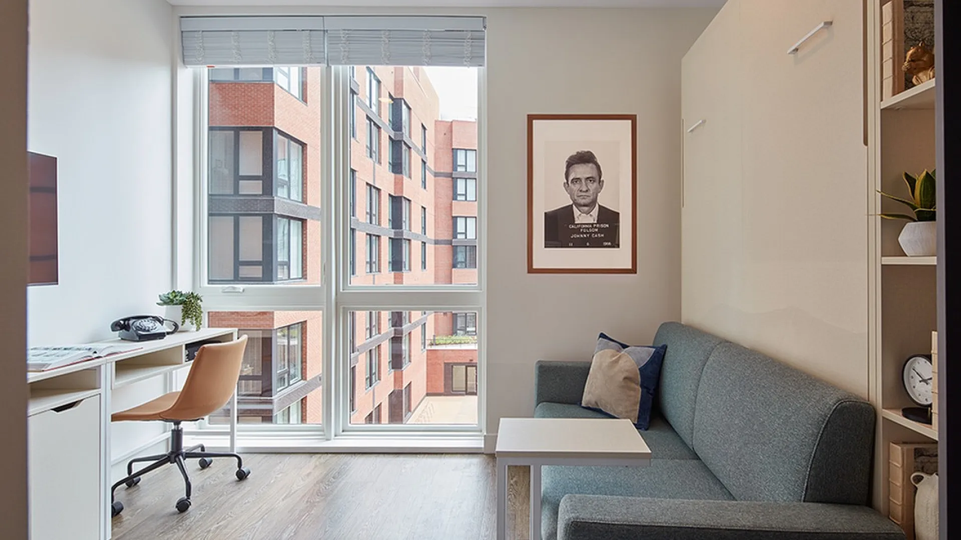 Bright apartment interior with a modern desk by large windows and a cozy sofa, offering a stylish urban view.