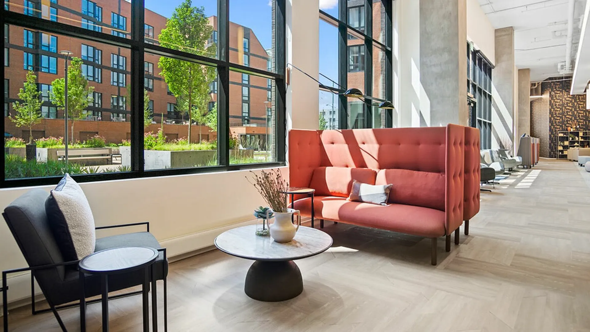 Bright and inviting modern lounge area with stylish seating, large windows showcasing lush greenery, and natural light flooding in.