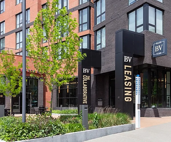 Modern apartment building exterior with sleek brick facade, lush landscaping, and inviting entrance for leasing opportunities.