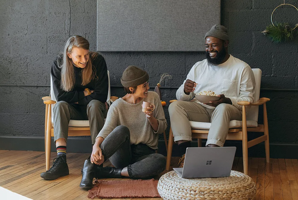 Cozy living room with cheerful people enjoying snacks and laughter, featuring modern decor and comfortable seating.