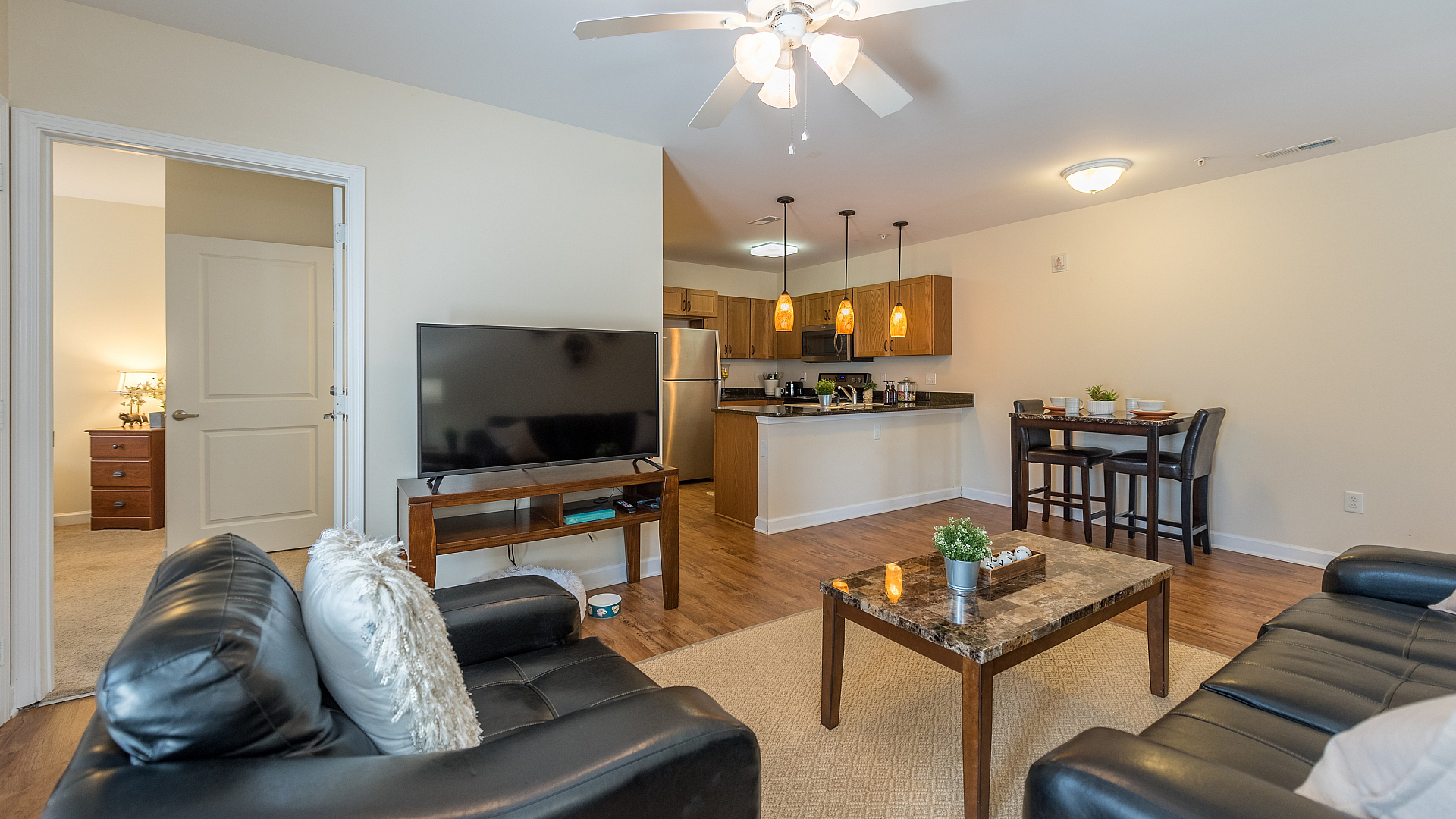 Modern open-concept living room featuring sleek black leather sofas, a cozy dining area, and a contemporary kitchen with stainless steel appliances and elegant pendant lighting.