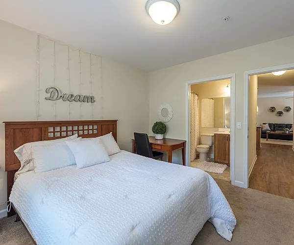 Inviting bedroom with cozy lighting, stylish wooden furniture, and a seamless transition to a modern en-suite bathroom, perfect for relaxation.