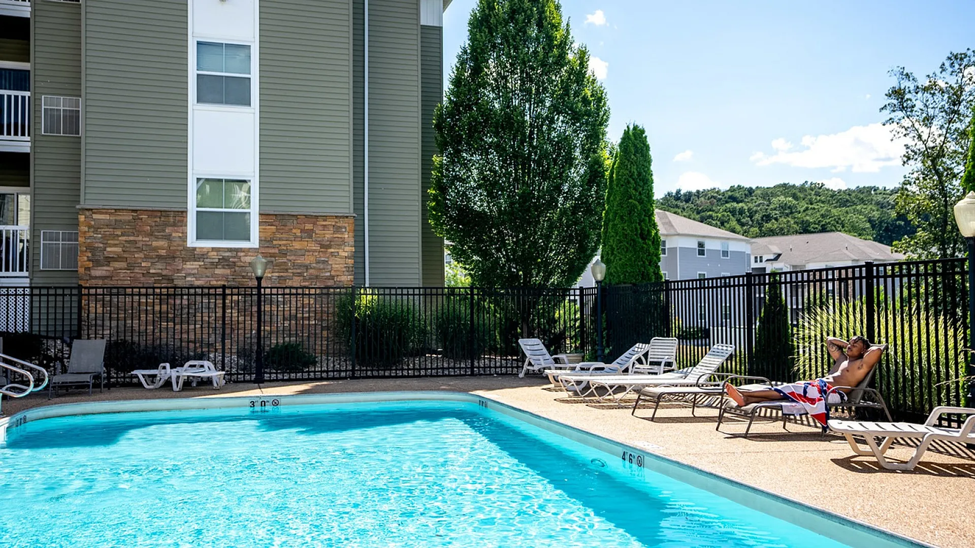 Inviting outdoor pool area with sun loungers and lush surroundings, perfect for relaxation at this modern apartment complex.